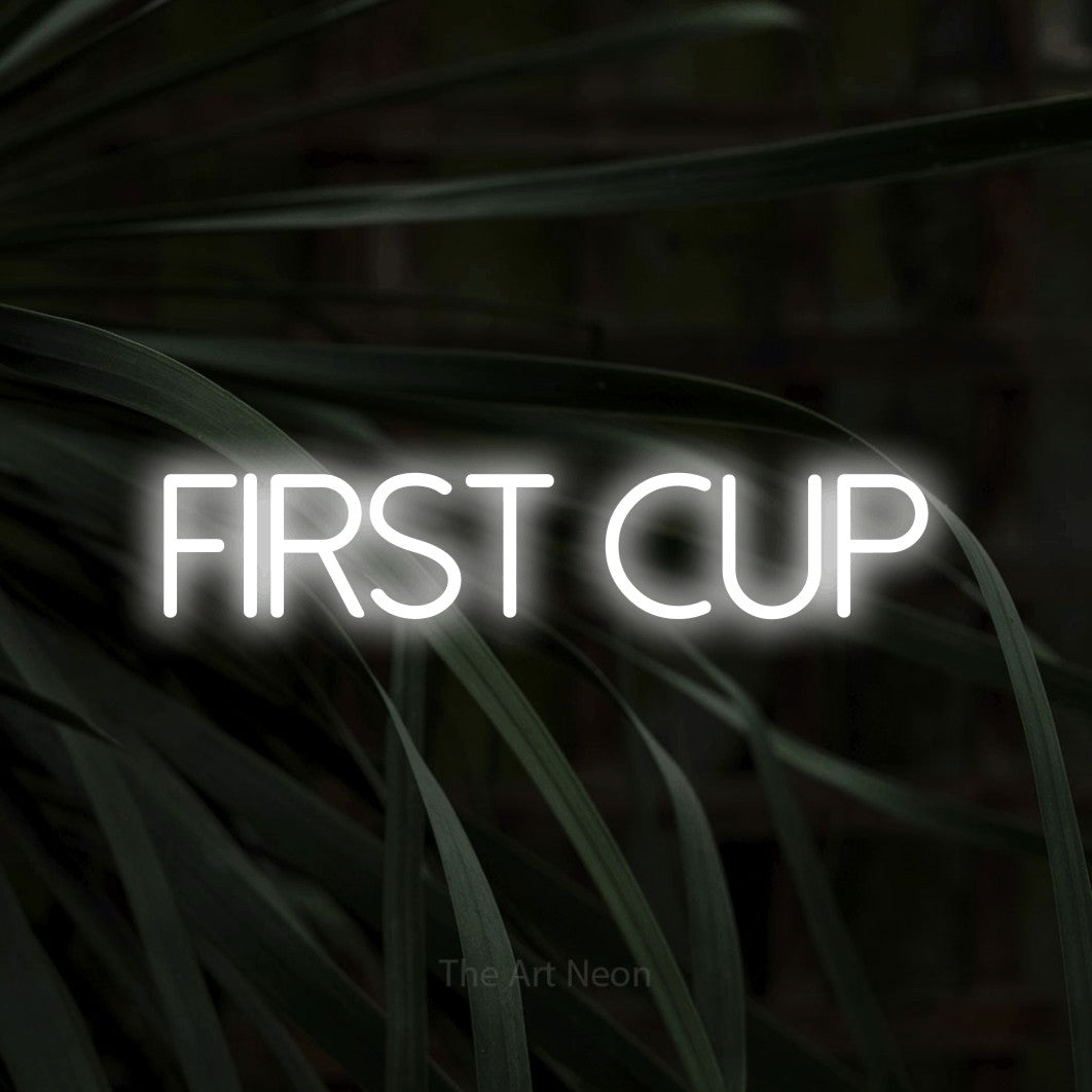 Cool white LED neon sign reading "First Cup" against dark tropical leaves for café décor