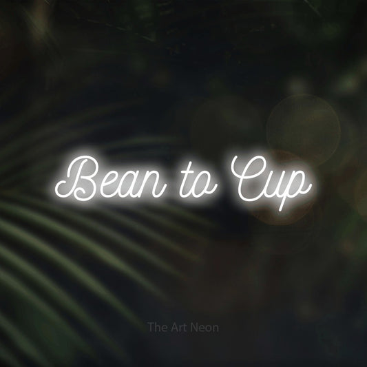 Cool white script-style LED neon sign reading "Bean to Cup" against dark blurred palm leaves for café décor
