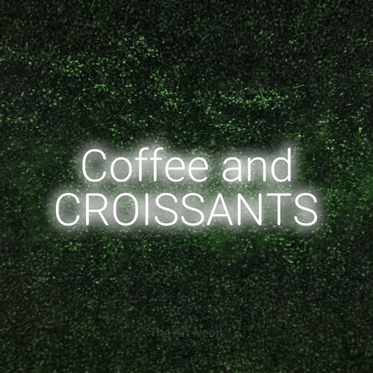 Cool white LED neon sign reading "Coffee and Croissants" against a textured green moss wall for café décor