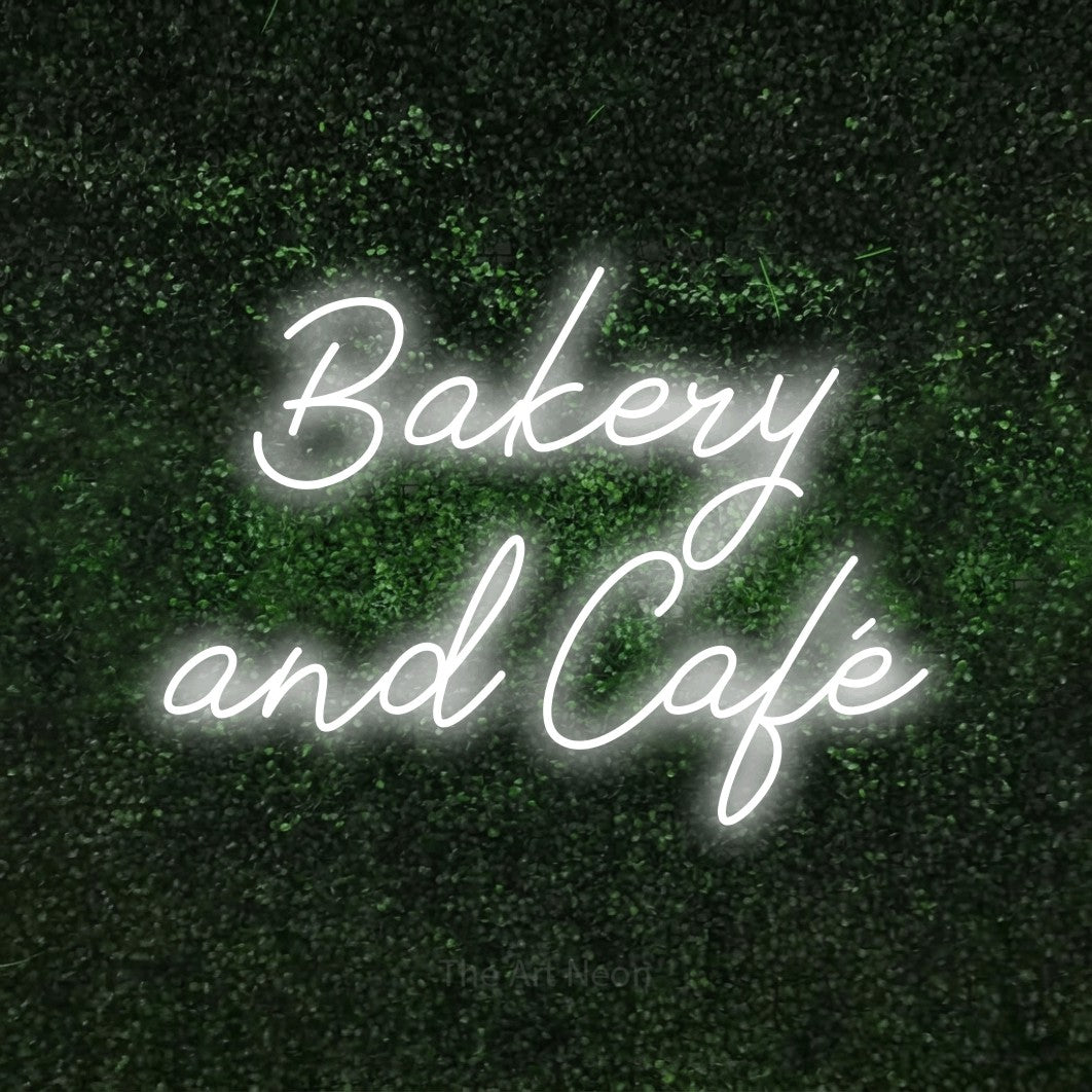 Cool white script-style LED neon sign reading "Bakery and Café" against a textured green moss wall for café décor