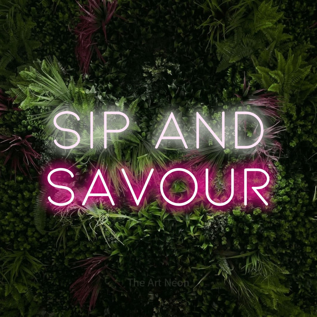 Hot pink and cool white LED neon sign reading "Sip and Savour" against a lush garden wall with pink flowers for café décor