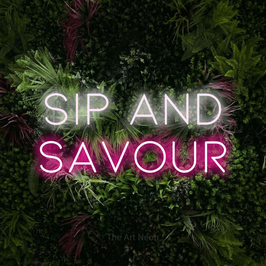 Hot pink and cool white LED neon sign reading "Sip and Savour" against a lush garden wall with pink flowers for café décor