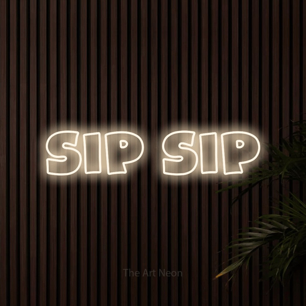 Warm white outline-style LED neon sign reading "Sip Sip" against dark wooden slats for café décor
