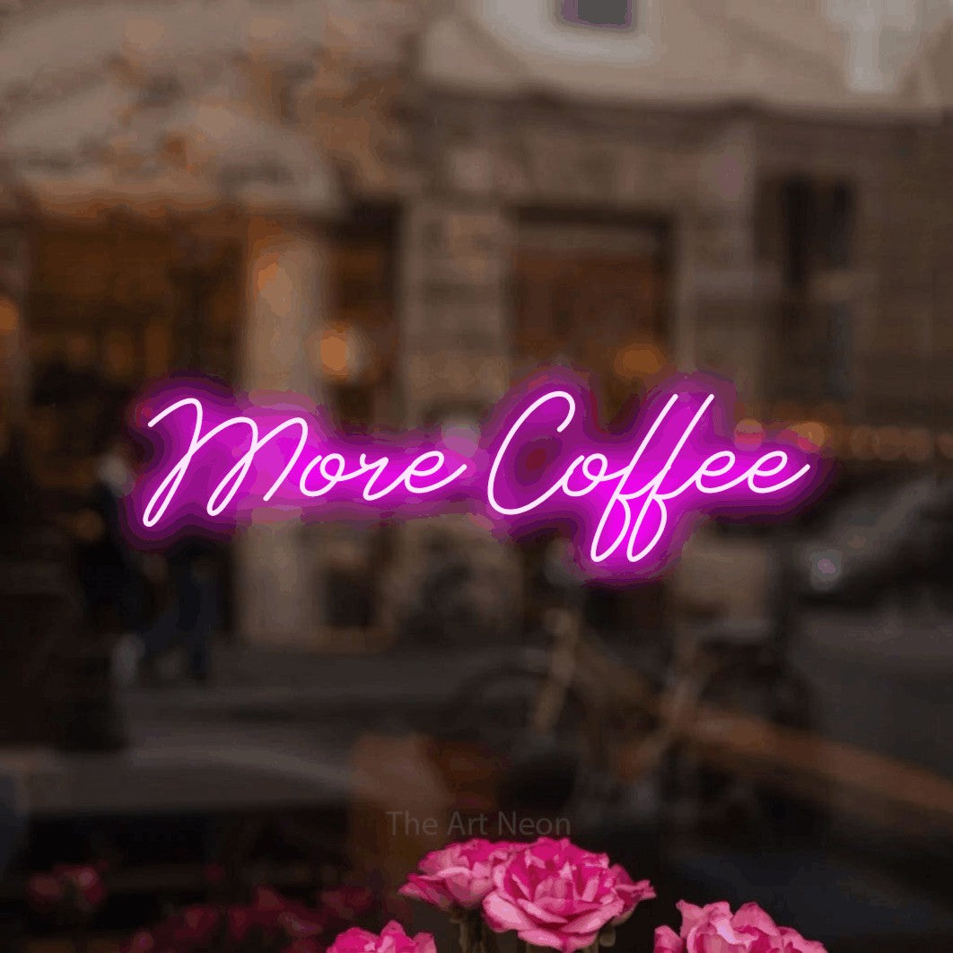 Pink script-style LED neon sign reading "More Coffee" in a softly blurred café interior for café décor