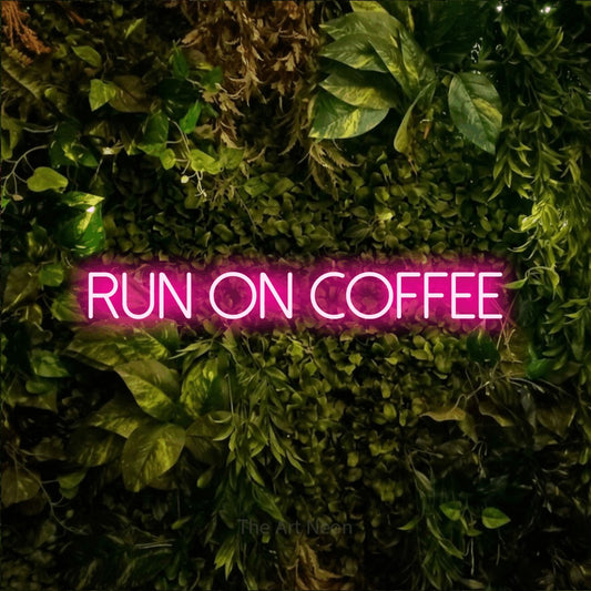 Hot pink LED neon sign reading "Run on Coffee" against a textured moss and foliage wall for café décor