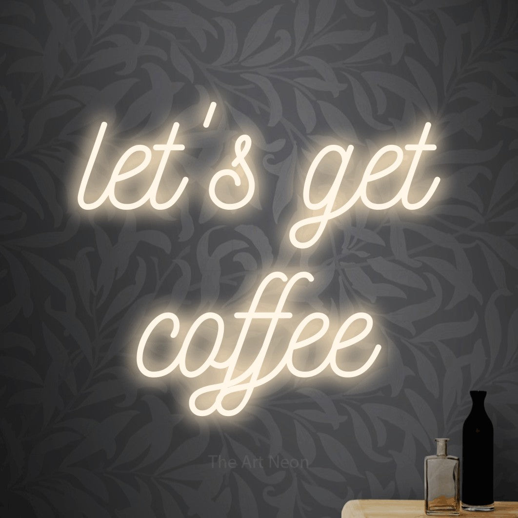 Warm white script-style LED neon sign reading "Let's Get Coffee" against light grey floral wallpaper for café décor