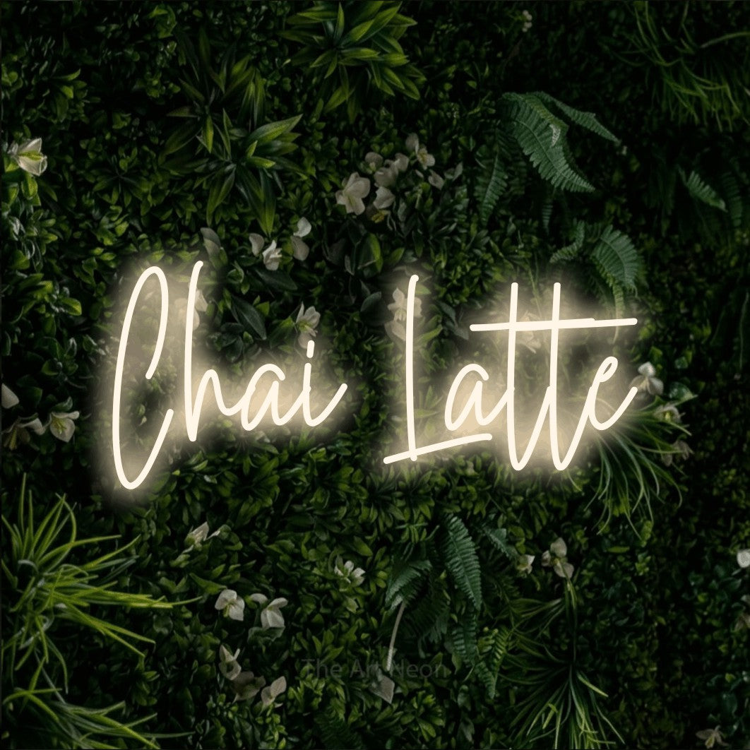 Warm white script-style LED neon sign reading "Chai Latte" against a leafy green wall for café décor