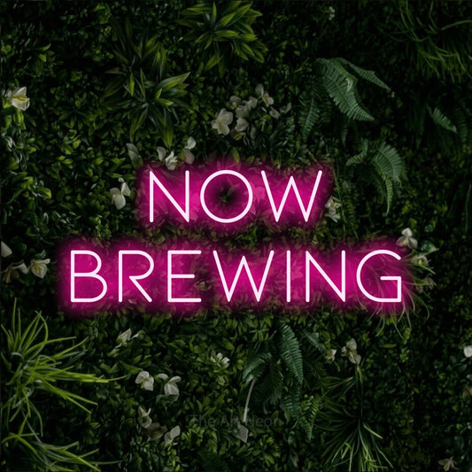 Hot pink LED neon sign reading "Now Brewing" against a leafy green wall for café décor