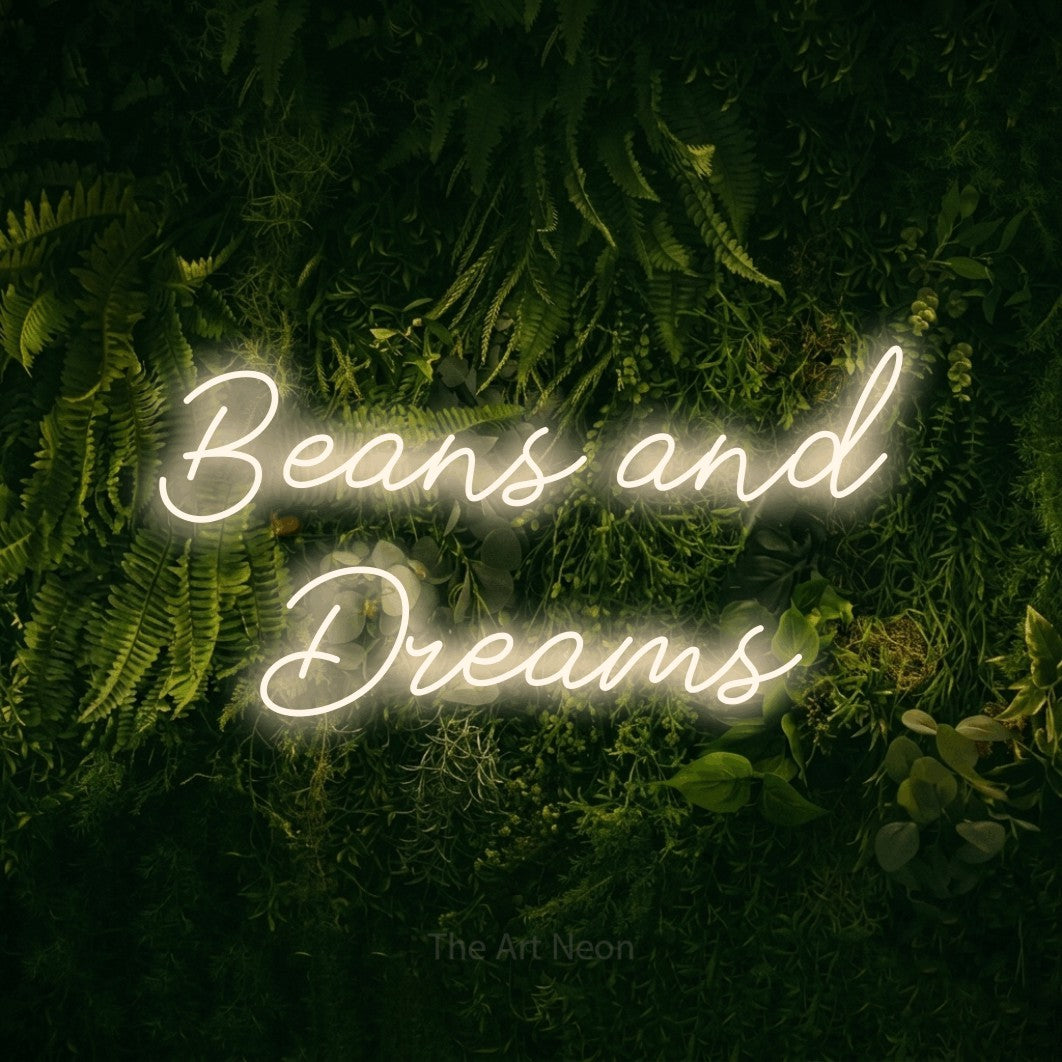 Warm white script-style LED neon sign reading "Beans and Dreams" against a moss-covered green wall for café décor