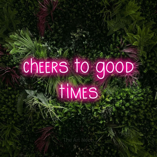Hot pink LED neon sign reading "Cheers to Good Times" against a lush garden wall with pink flowers for bar décor