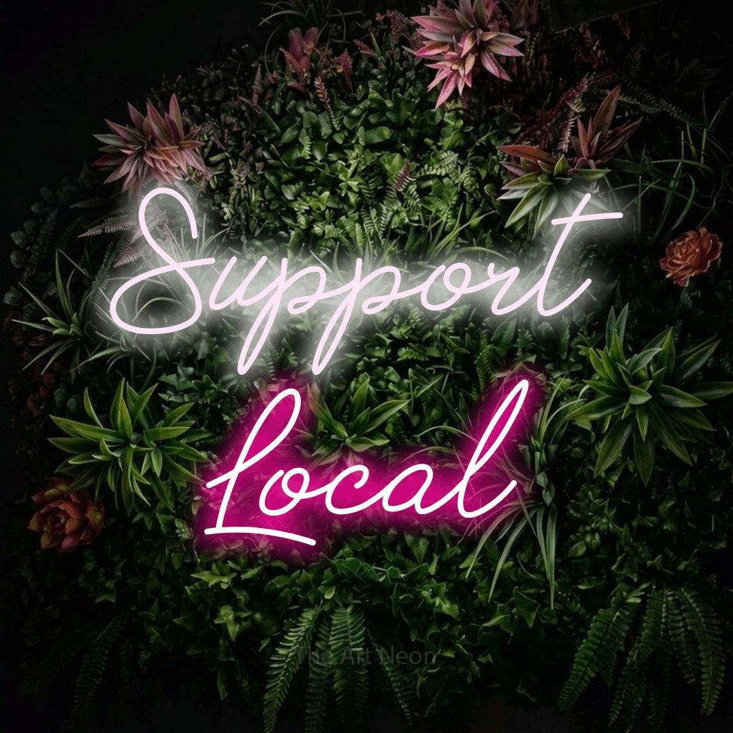 Hot pink and cool white script-style LED neon sign reading "Support Local" against a flowering garden wall for bar décor