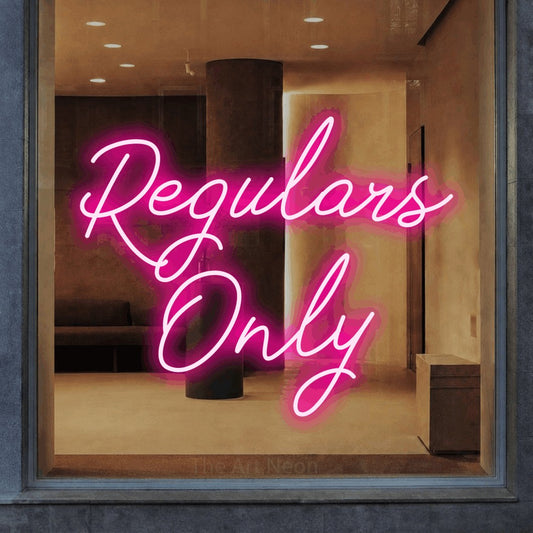 Hot pink script-style LED neon sign reading "Regulars Only" in a warm modern interior for bar décor