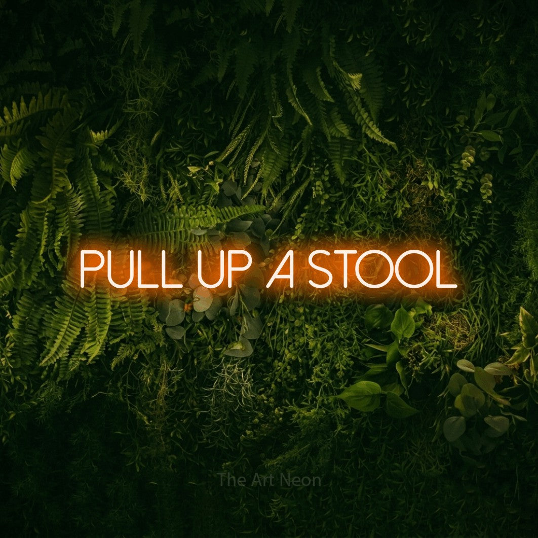 Orange LED neon sign reading "Pull Up a Stool" against a moss-covered green wall for bar décor
