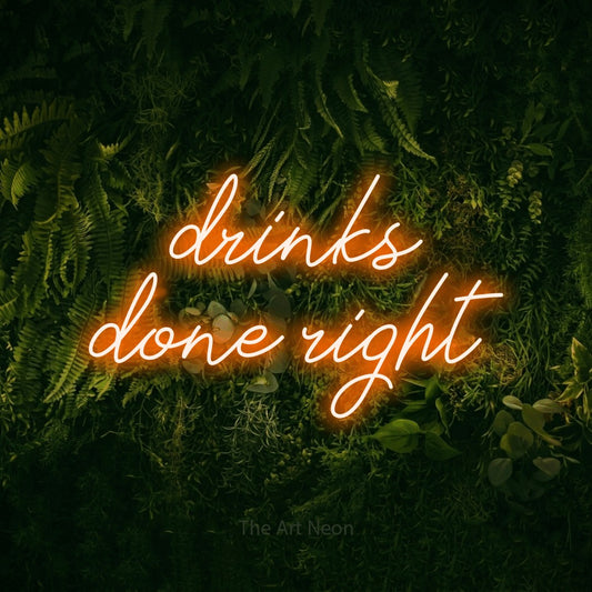 Orange script-style LED neon sign reading "Drinks Done Right" against a moss-covered green wall for bar décor