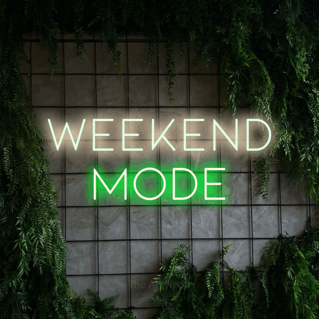 Green and warm white LED neon sign reading "Weekend Mode" against a green grid wall with foliage for bar décor