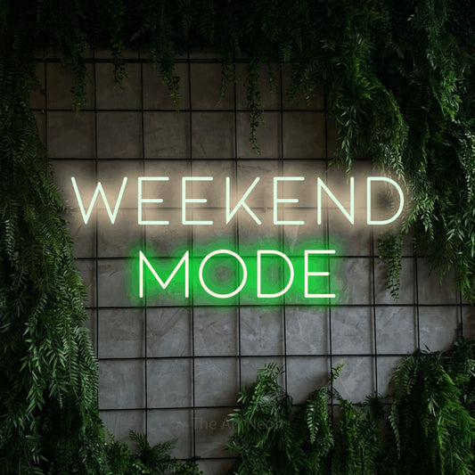 Green and warm white LED neon sign reading "Weekend Mode" against a green grid wall with foliage for bar décor
