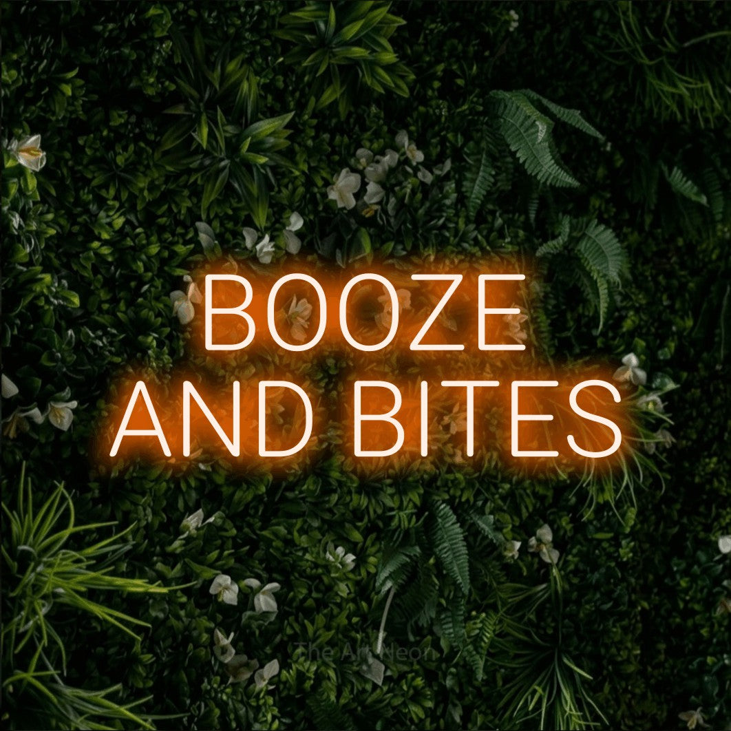 Orange LED neon sign reading "Booze and Bites" against a leafy green wall for bar décor