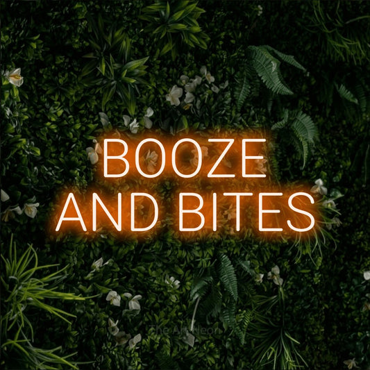 Orange LED neon sign reading "Booze and Bites" against a leafy green wall for bar décor