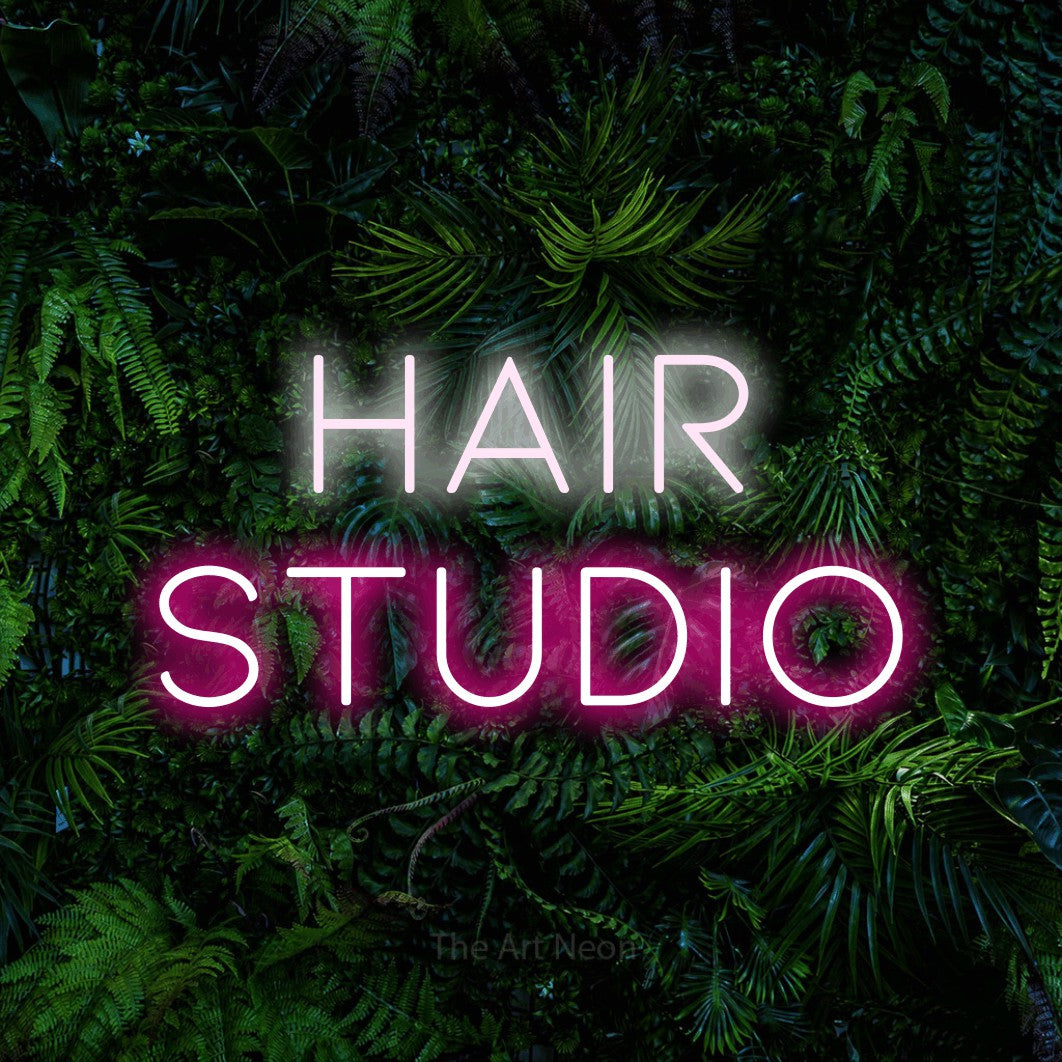 Hot pink and cool white LED neon sign reading "Hair Studio" against a dense tropical foliage wall for salon décor