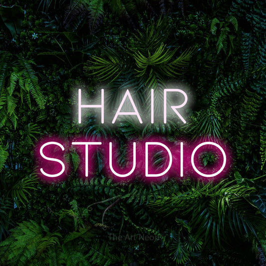 Hot pink and cool white LED neon sign reading "Hair Studio" against a dense tropical foliage wall for salon décor
