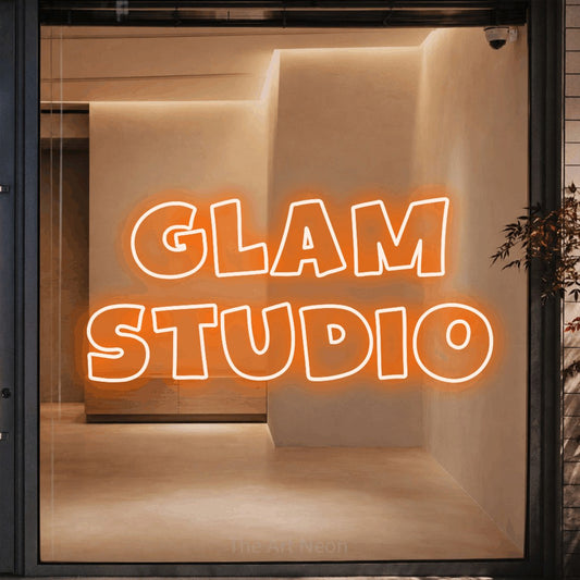 Orange outline-style LED neon sign reading "Glam Studio" against a warm beige alcove wall for salon décor