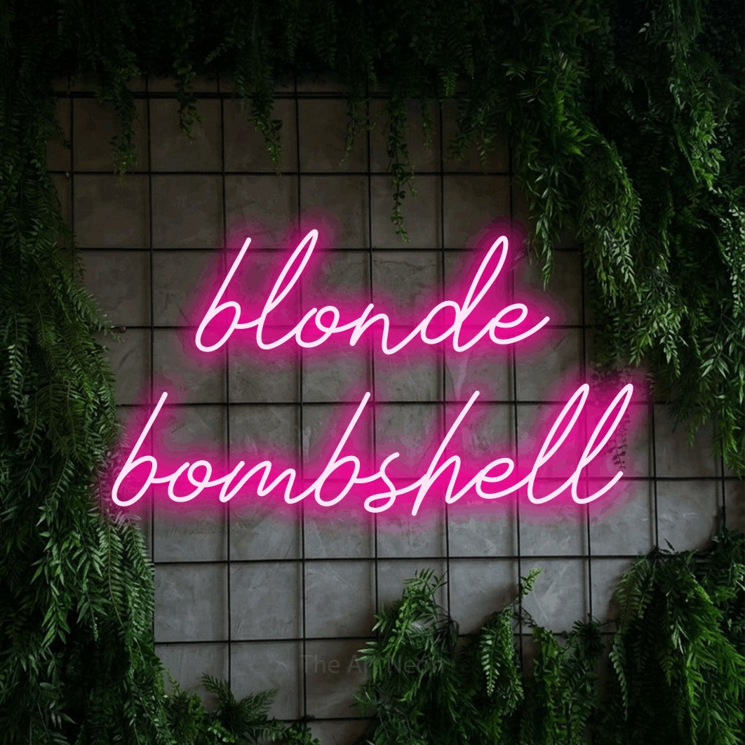 Hot pink script-style LED neon sign reading "Blonde Bombshell" against a green grid wall with foliage for salon décor