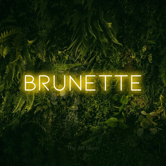 Yellow LED neon sign reading "Brunette" against a moss-covered green wall for salon décor