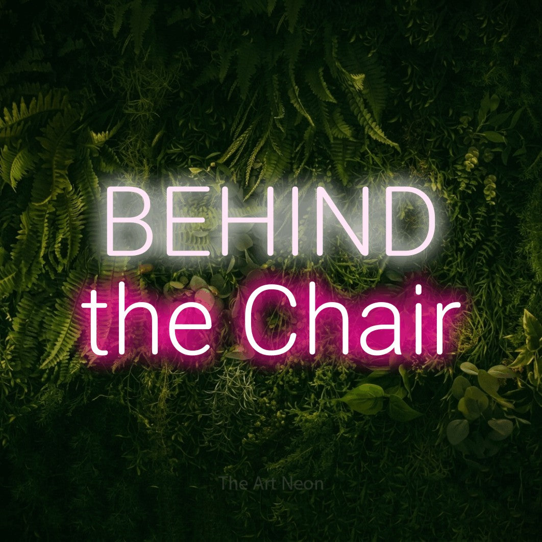 Hot pink and cool white LED neon sign reading "Behind the Chair" against a moss-covered green wall for salon décor