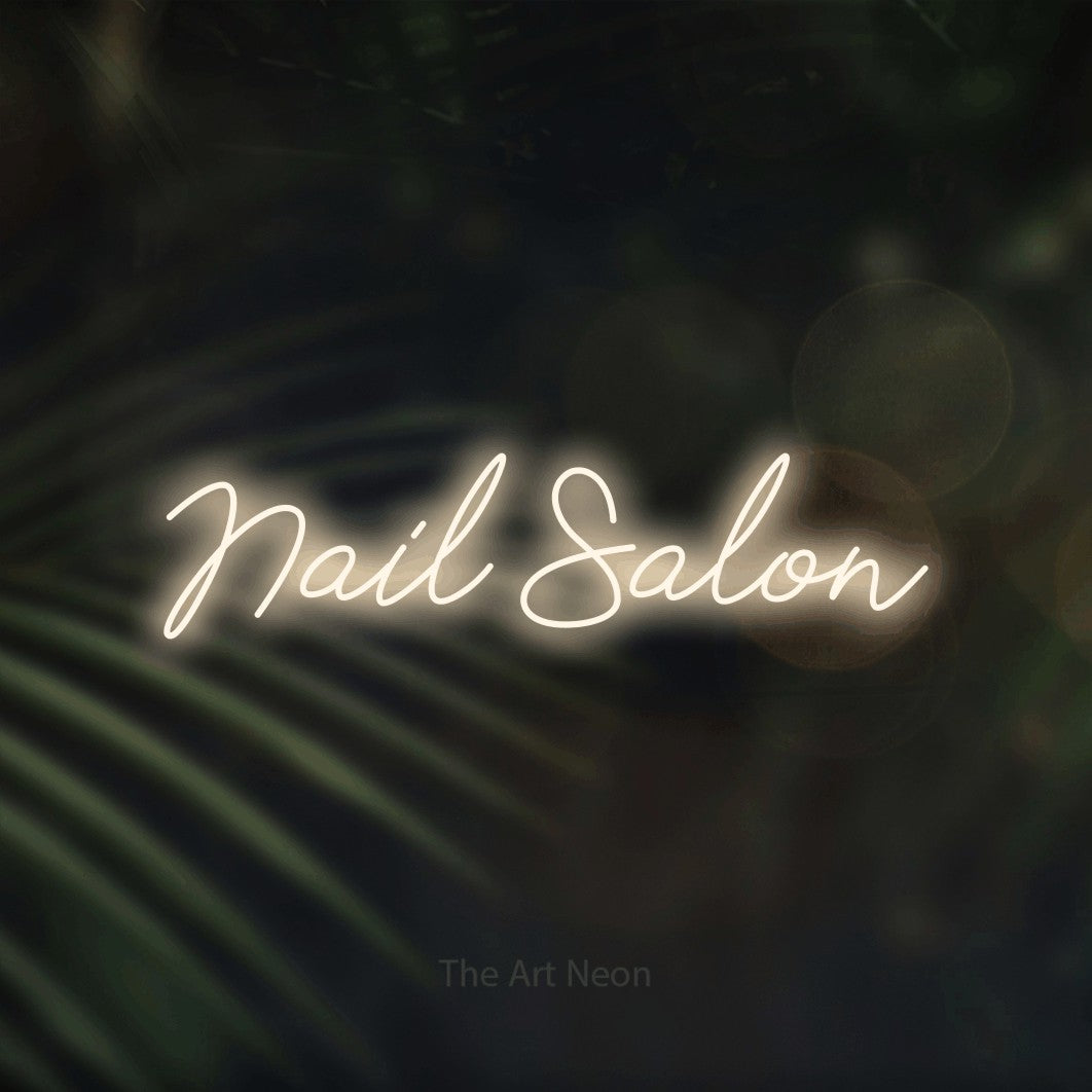 Warm white script-style LED neon sign reading "Nail Salon" against dark blurred palm leaves for salon décor
