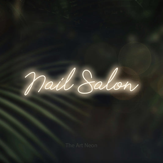 Warm white script-style LED neon sign reading "Nail Salon" against dark blurred palm leaves for salon décor
