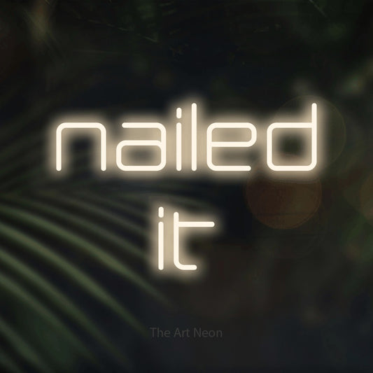 Warm white LED neon sign reading "Nailed It" against dark blurred palm leaves for salon décor