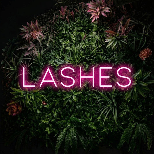 Hot pink LED neon sign reading "Lashes" against a flowering garden wall for salon décor