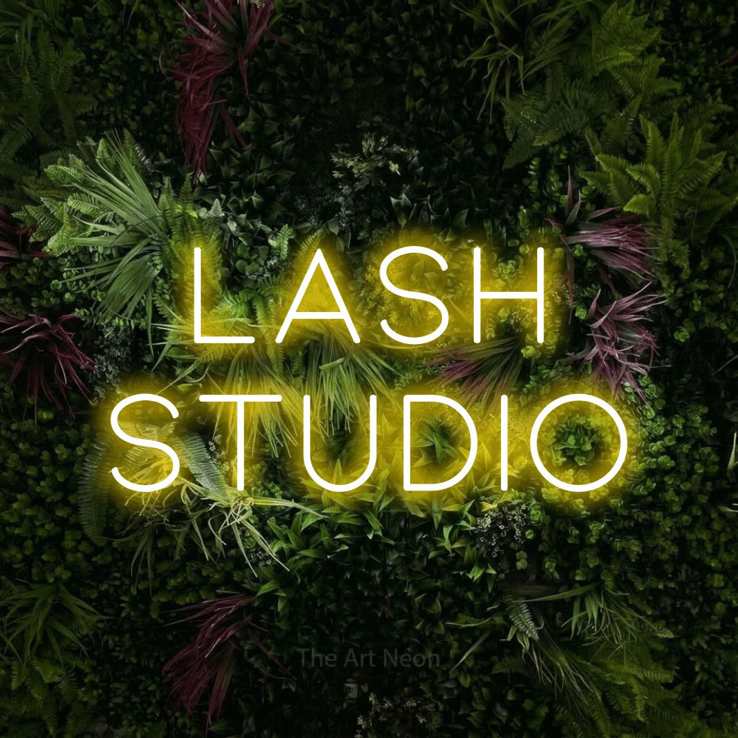 Yellow LED neon sign reading "Lash Studio" against a lush garden wall with pink flowers for salon décor
