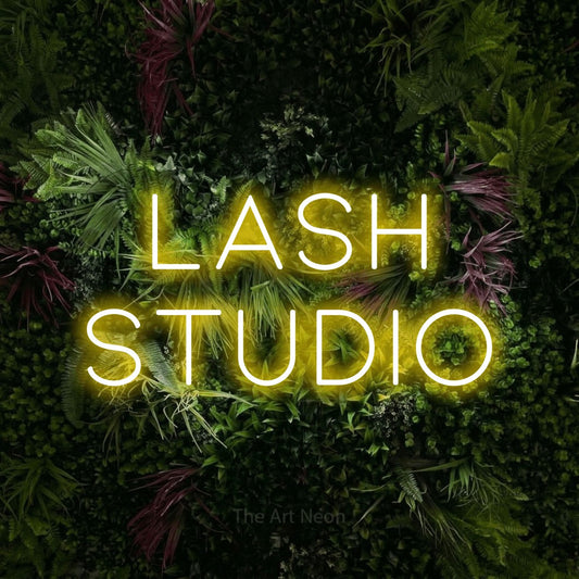 Yellow LED neon sign reading "Lash Studio" against a lush garden wall with pink flowers for salon décor
