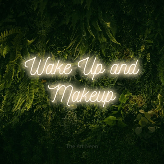 Warm white script-style LED neon sign reading "Wake Up and Makeup" against a moss-covered green wall for salon décor