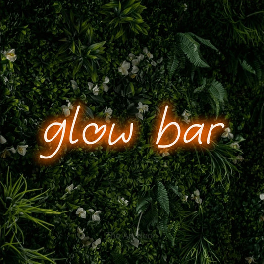 Orange LED neon sign reading "Glow Bar" against a leafy green wall for salon décor