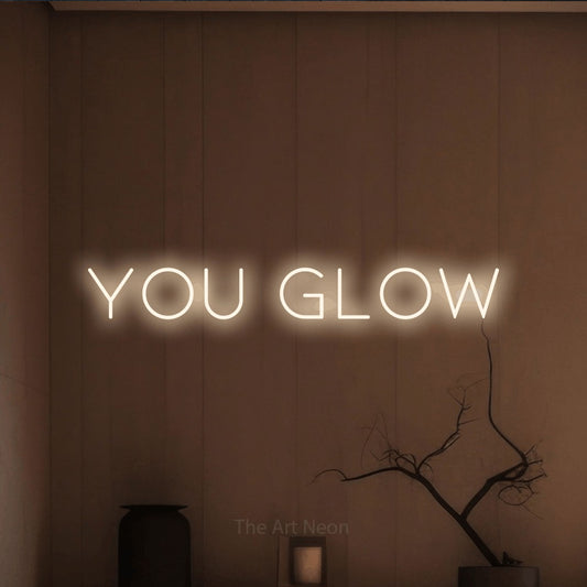 Warm white LED neon sign reading "You Glow" against a warm brown wall for salon décor