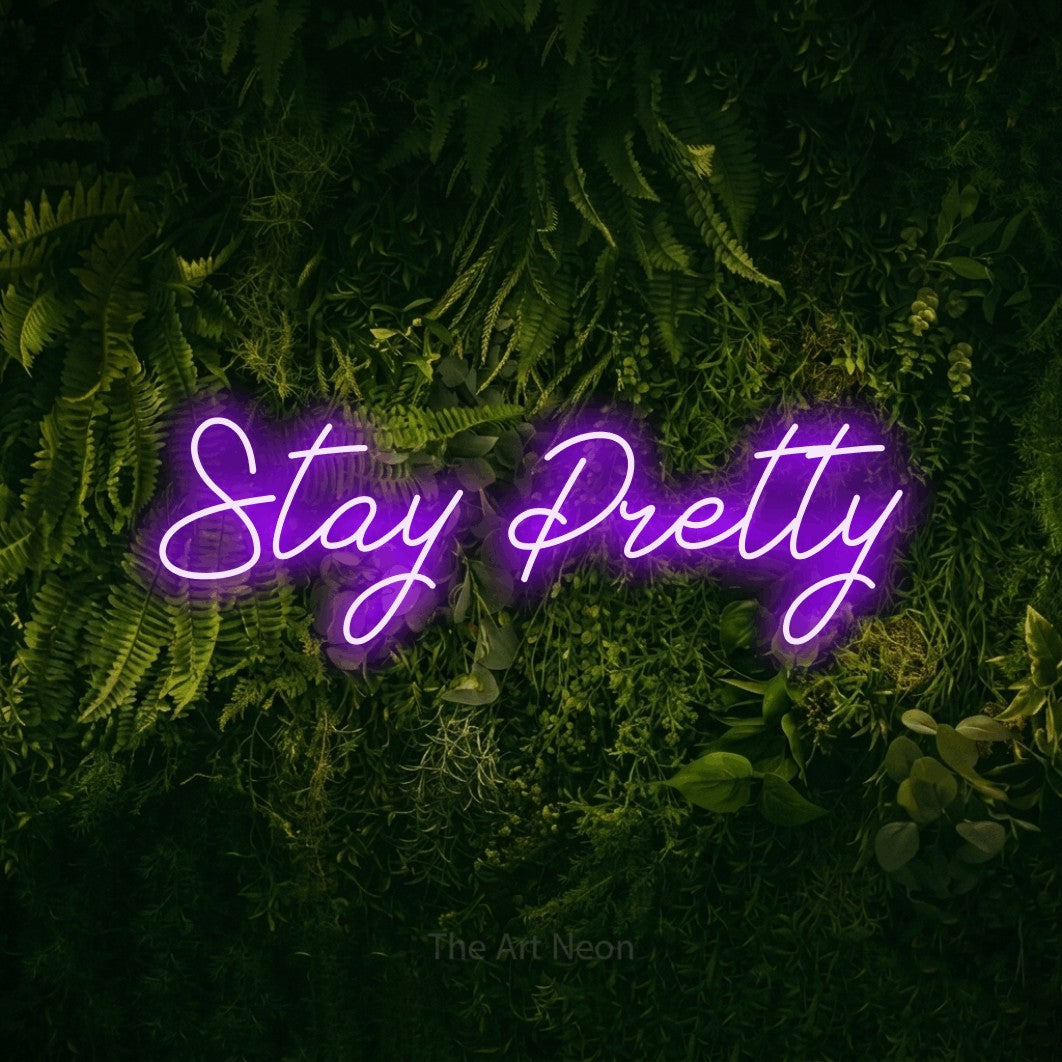 Purple script-style LED neon sign reading "Stay Pretty" against a moss-covered green wall for salon décor
