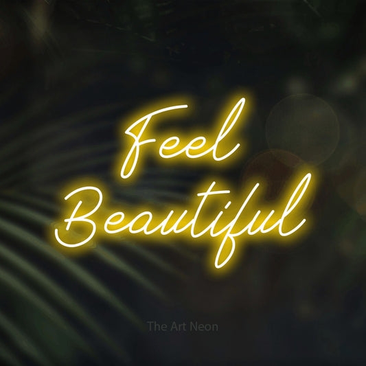 Yellow script-style LED neon sign reading "Feel Beautiful" against dark blurred palm leaves for salon décor