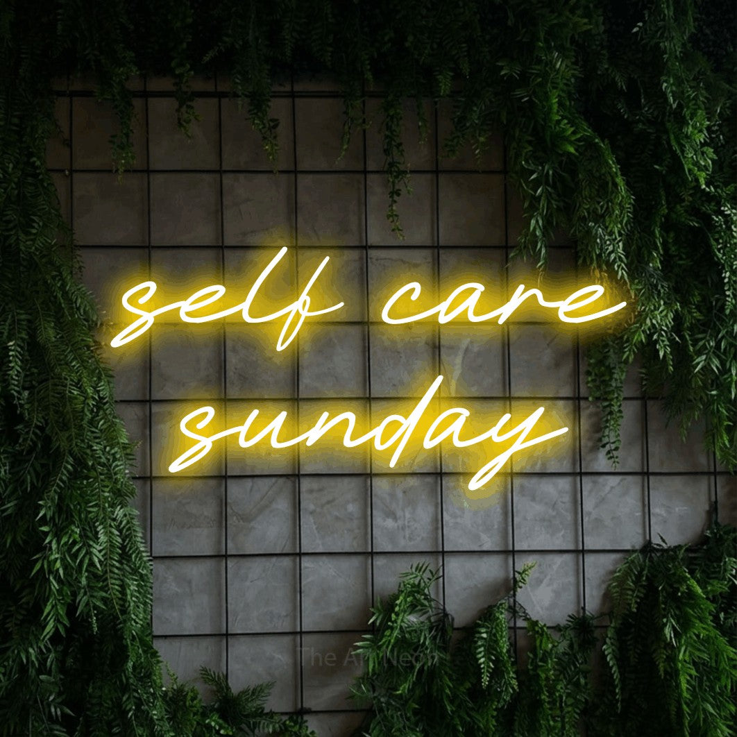 Yellow LED neon sign reading "Self Care Sunday" against a green grid wall with foliage for salon décor