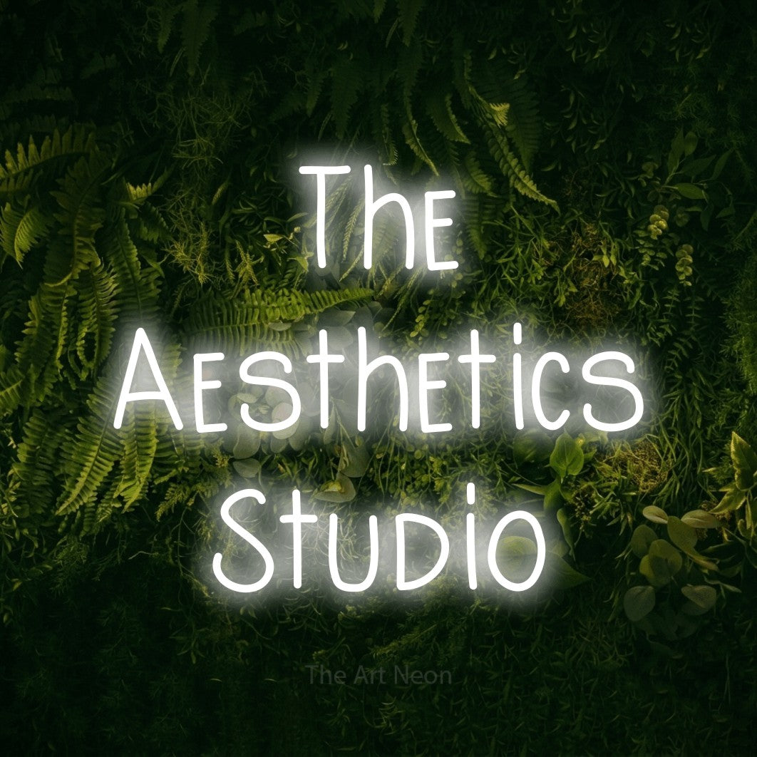Cool white LED neon sign reading "The Aesthetics Studio" against a moss-covered green wall for salon décor