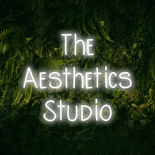 Cool white LED neon sign reading "The Aesthetics Studio" against a moss-covered green wall for salon décor
