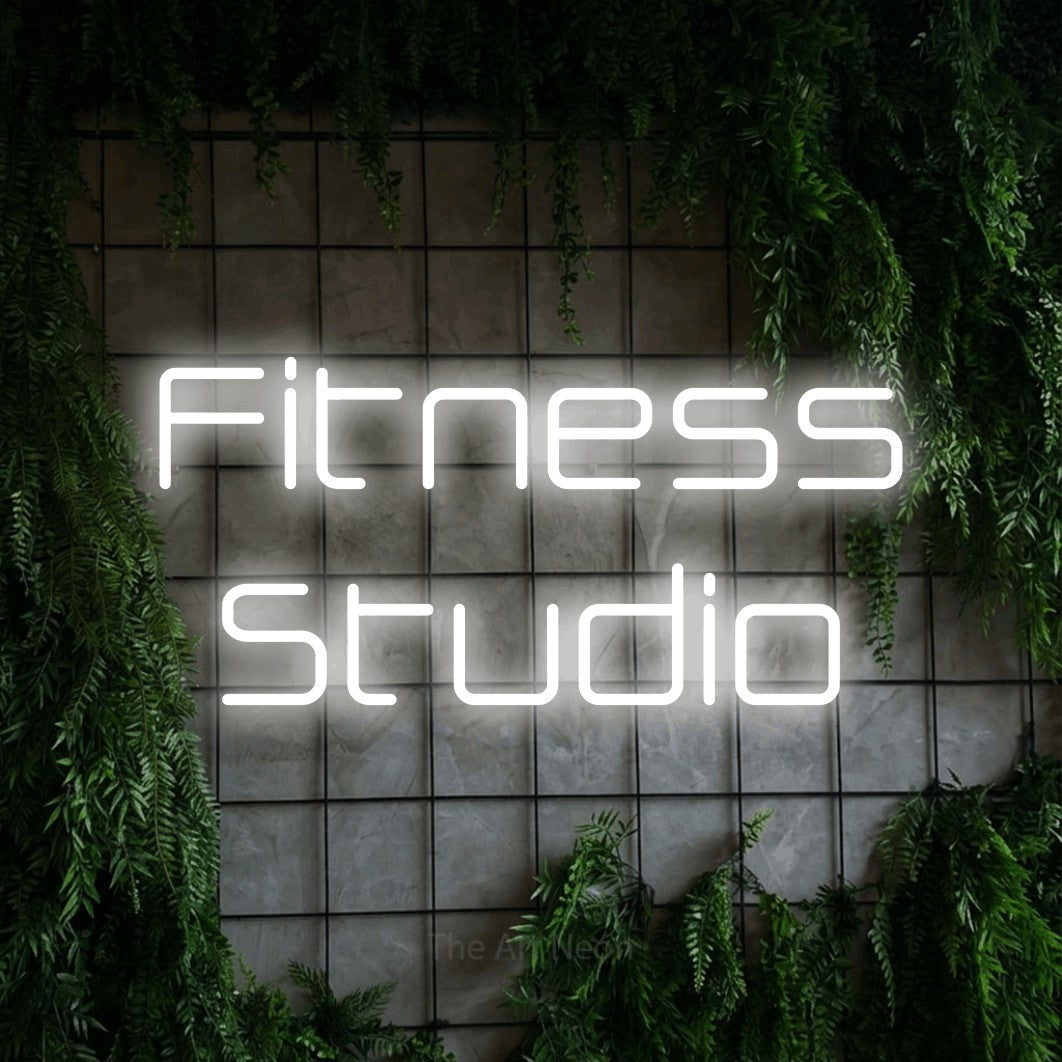 Cool white LED neon sign reading "Fitness Studio" against a green grid wall with foliage for gym décor
