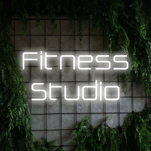 Enseigne néon à DEL à lumière blanche froide, affichant « Fitness Studio » sur un mur quadrillé vert avec du feuillage, pour décorer une salle d’entraînement