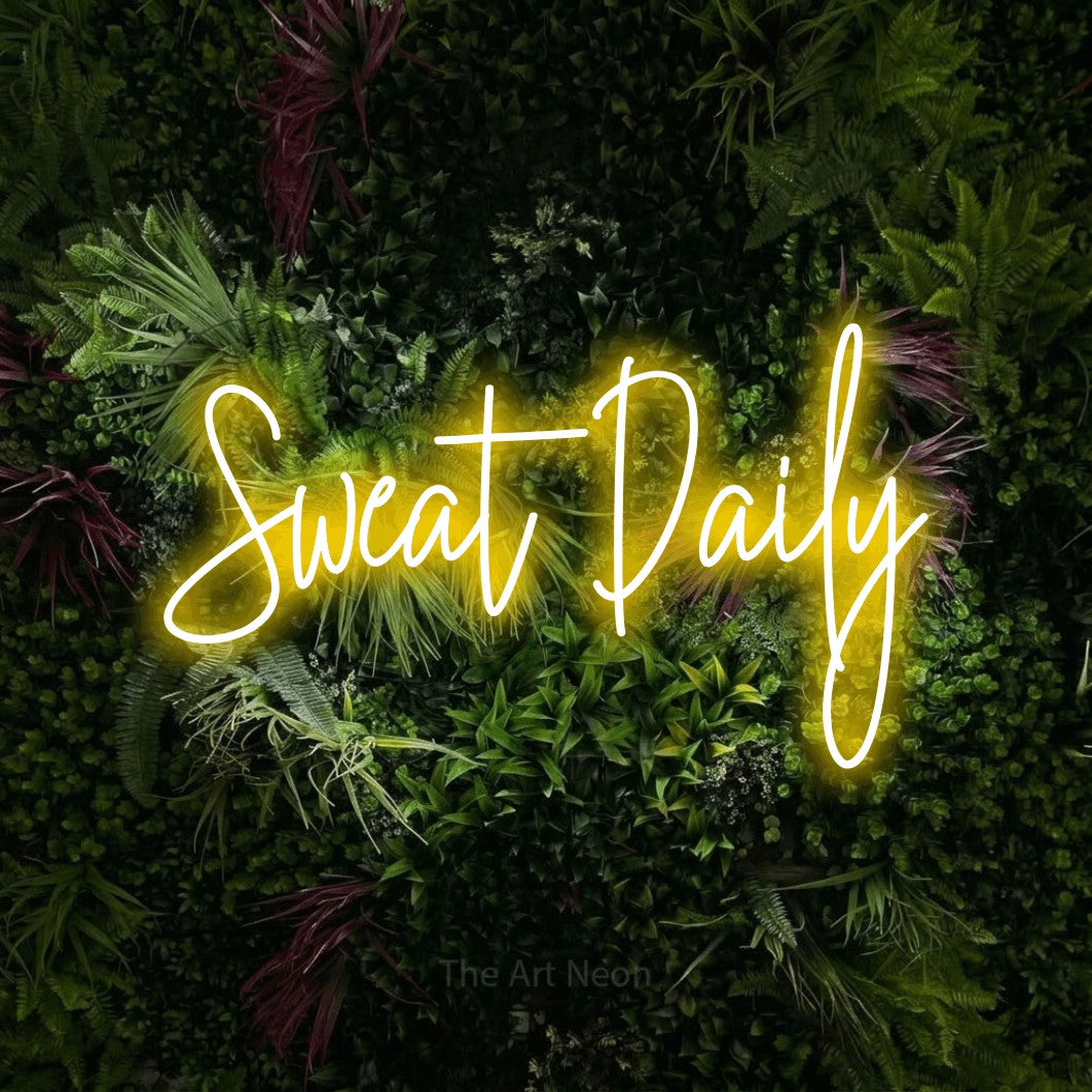 Yellow script-style LED neon sign reading "Sweat Daily" against a lush garden wall with pink flowers for gym décor