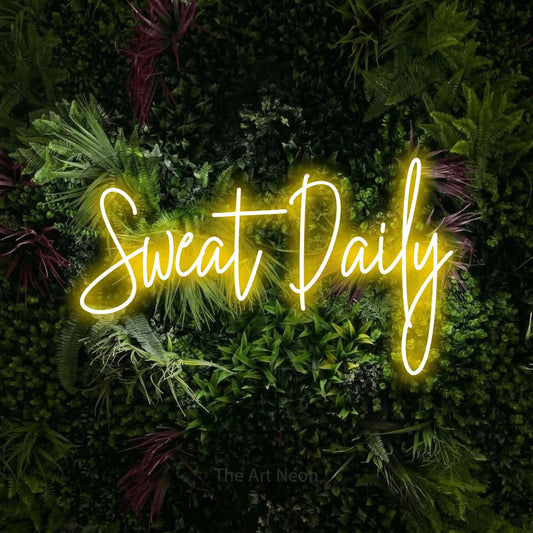 Enseigne néon à DEL à lumière jaune, de style manuscrit, affichant « Sweat Daily » sur un mur de jardin luxuriant aux fleurs roses, pour décorer une salle d’entraînement