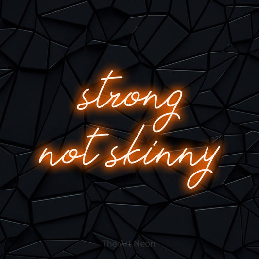 Orange script-style LED neon sign reading "Strong Not Skinny" against a black faceted wall for gym décor