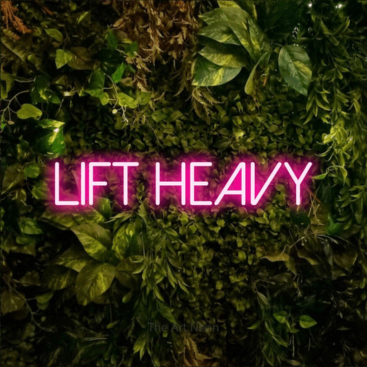Hot pink LED neon sign reading "Lift Heavy" against a textured moss and foliage wall for gym décor