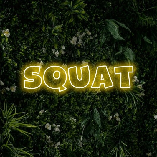 Yellow outline-style LED neon sign reading "Squat" against a leafy green wall for gym décor