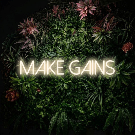 Warm white LED neon sign reading "Make Gains" against a flowering garden wall for gym décor